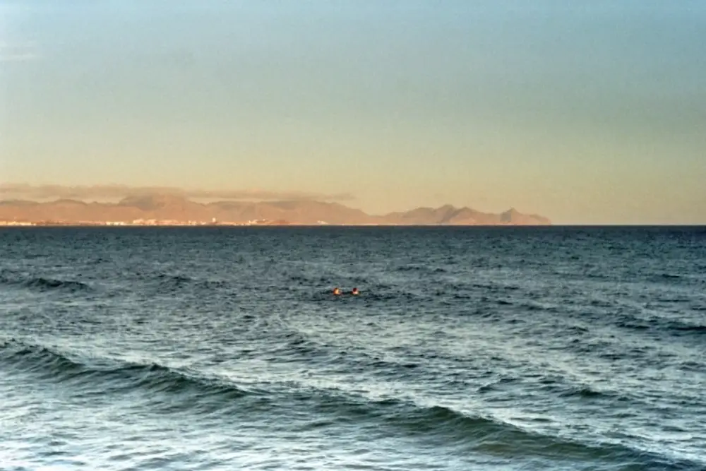 Zwei Menschen schwimmen im Meer. Im Hintergrund sind Berge in der Abenddämmerung zu sehen